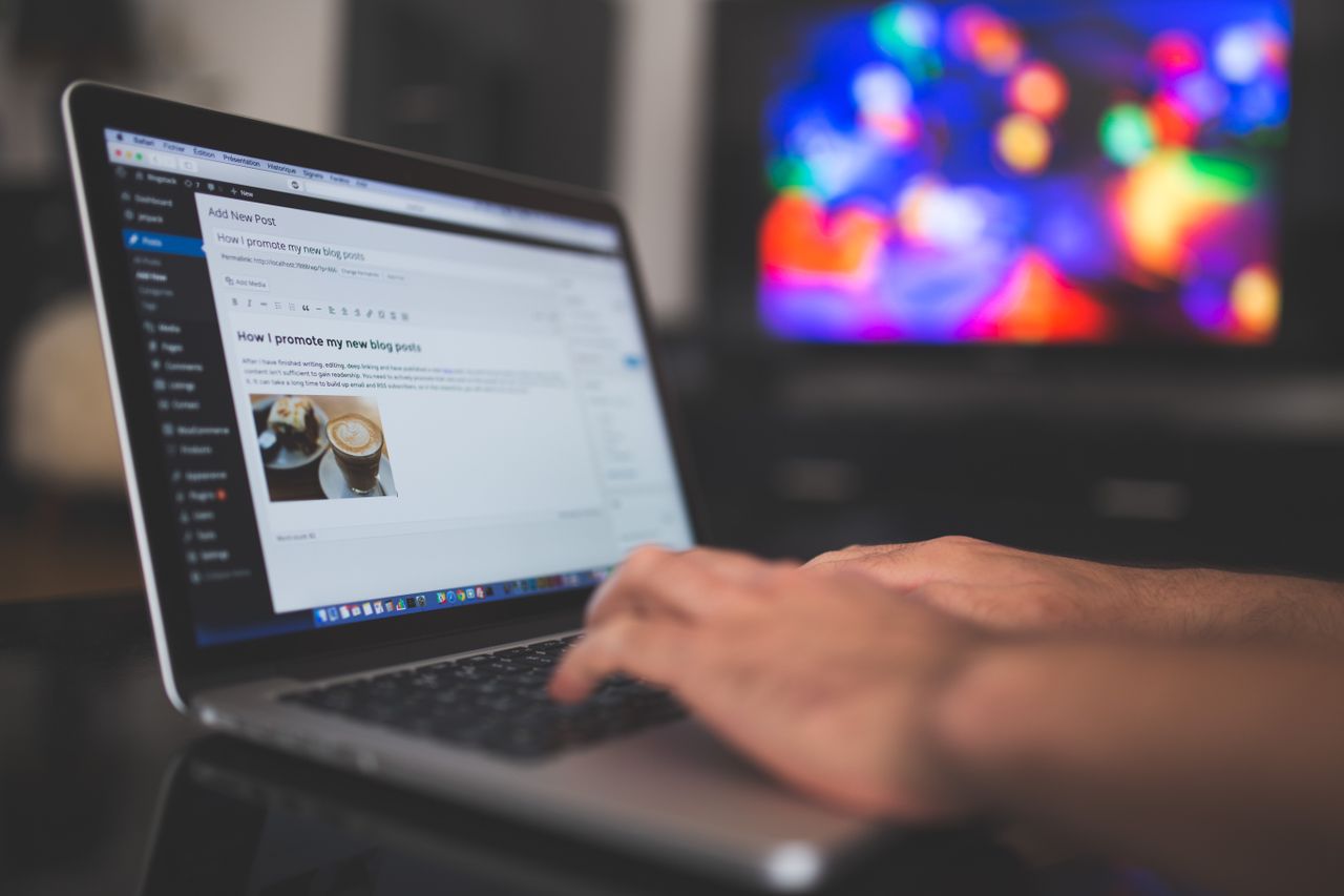 The Art of Drawing Readers In: Your attractive post title goes here Hands typing on a laptop with a blog post visible, cozy indoor setting with colorful screen in background.